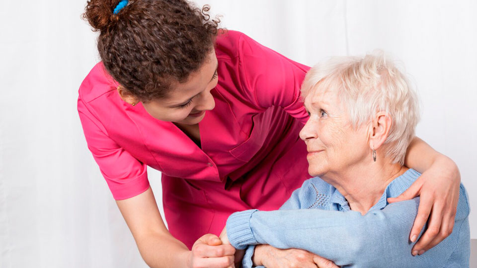 Pflegekraft und ältere Frau schauen sich lächelnd an