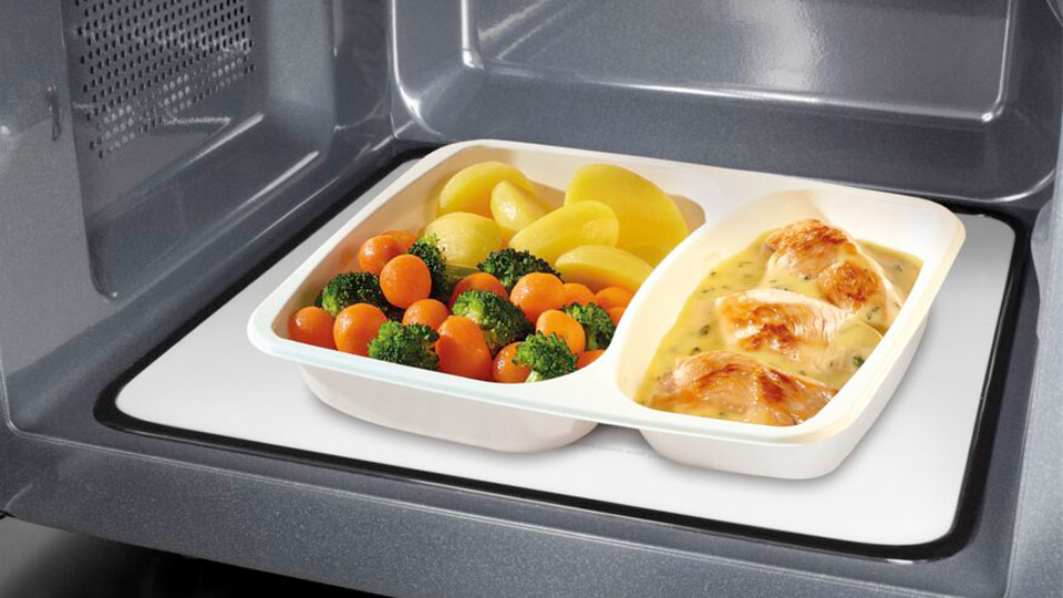 Fertiggericht mit Gemüse, Kartoffeln und Hähnchen in einer Plastikschale auf dem Drehteller einer Mikrowelle