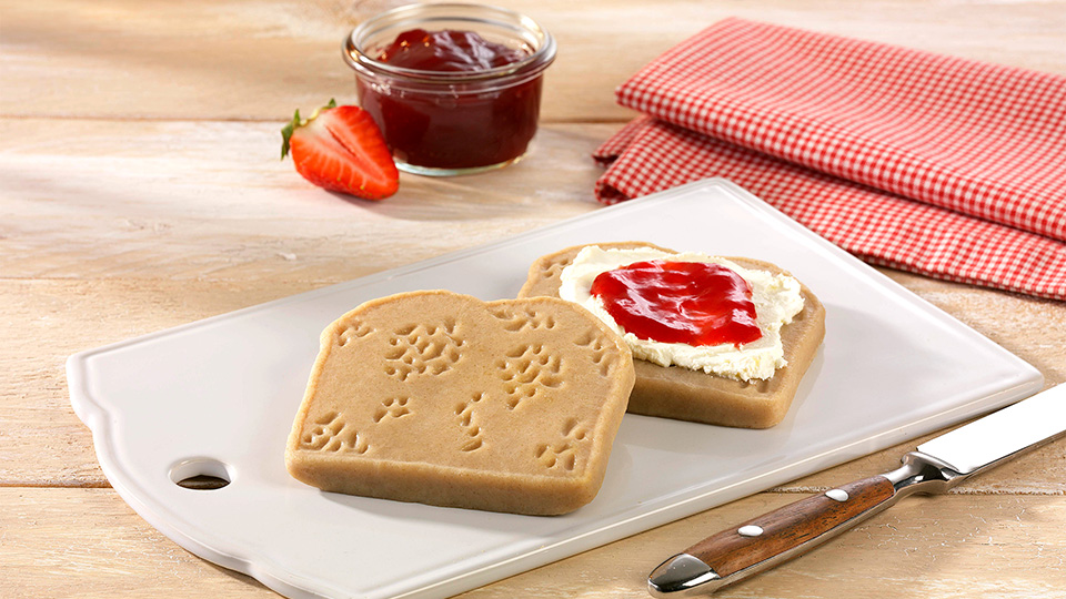 Pürierte Brotzeitschnitte in Form von Brotscheiben, eine davon bestrichen mit Quark und Erdbeermarmelade