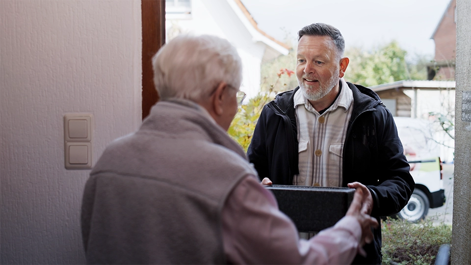 Ein Menükurier steht an der Tür und überreicht der Seniorin ihr Menü