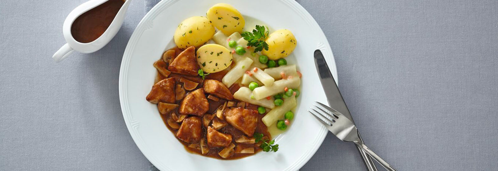 Hähnchenfilet in Pilzsoße, Kartoffeln, Spargel mit Erbsen und Petersilie, daneben eine Sauciere mit Soße