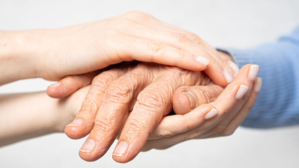 Zwei jüngere Hände halten die Hand einer älteren Person